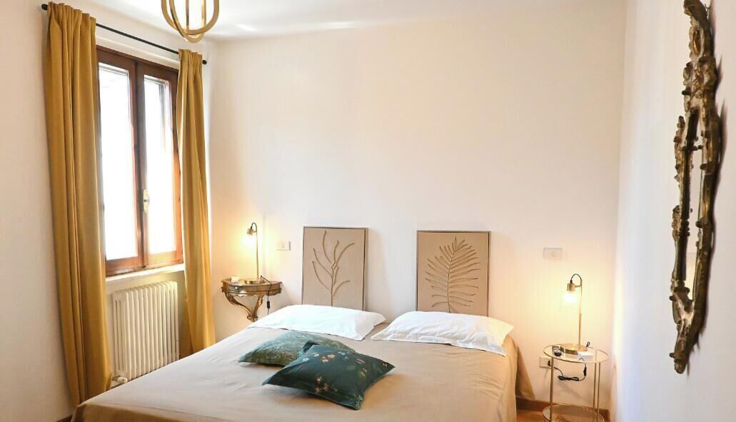 A bedroom with a bed, two bedside tables, a window with curtains, and wall art.