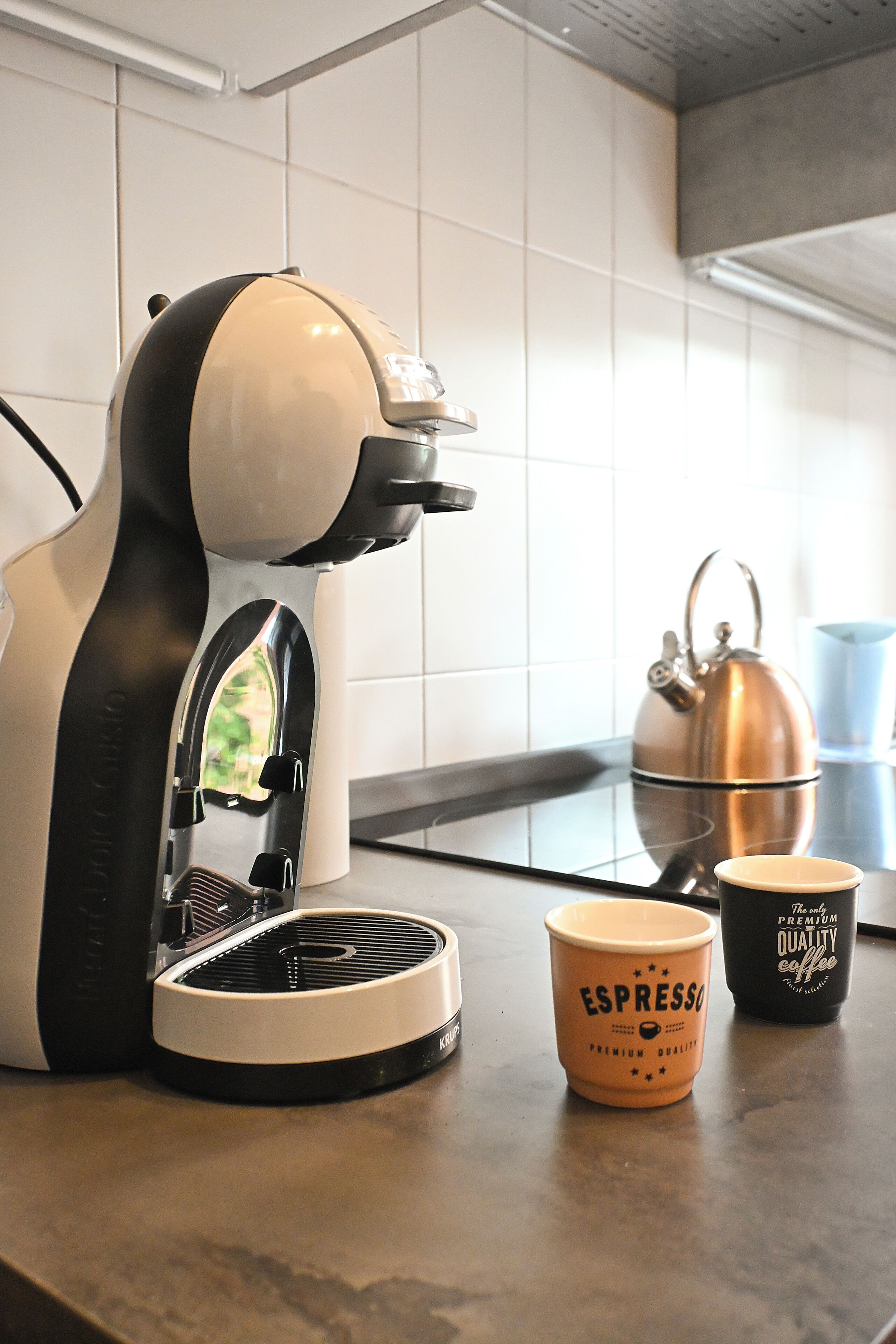 Una cocina con cafetera, hervidor y dos tazas sobre la encimera.