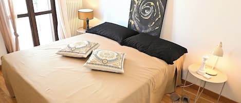 Habitación de hotel con cama, dos almohadas, un cuadro, una lámpara, pantuflas y una alfombra.