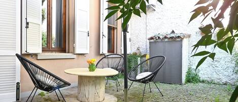 Une cour avec une table ronde, deux chaises et un pot de fleurs.