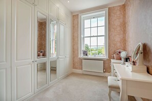 Ein Schlafzimmer mit großem Fenster, einem Schminktisch mit Spiegel und einem Kleiderschrank mit Spiegelüren.