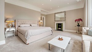 Een ruime slaapkamer met een groot bed, een open haard, een kroonluchter en een salontafel.