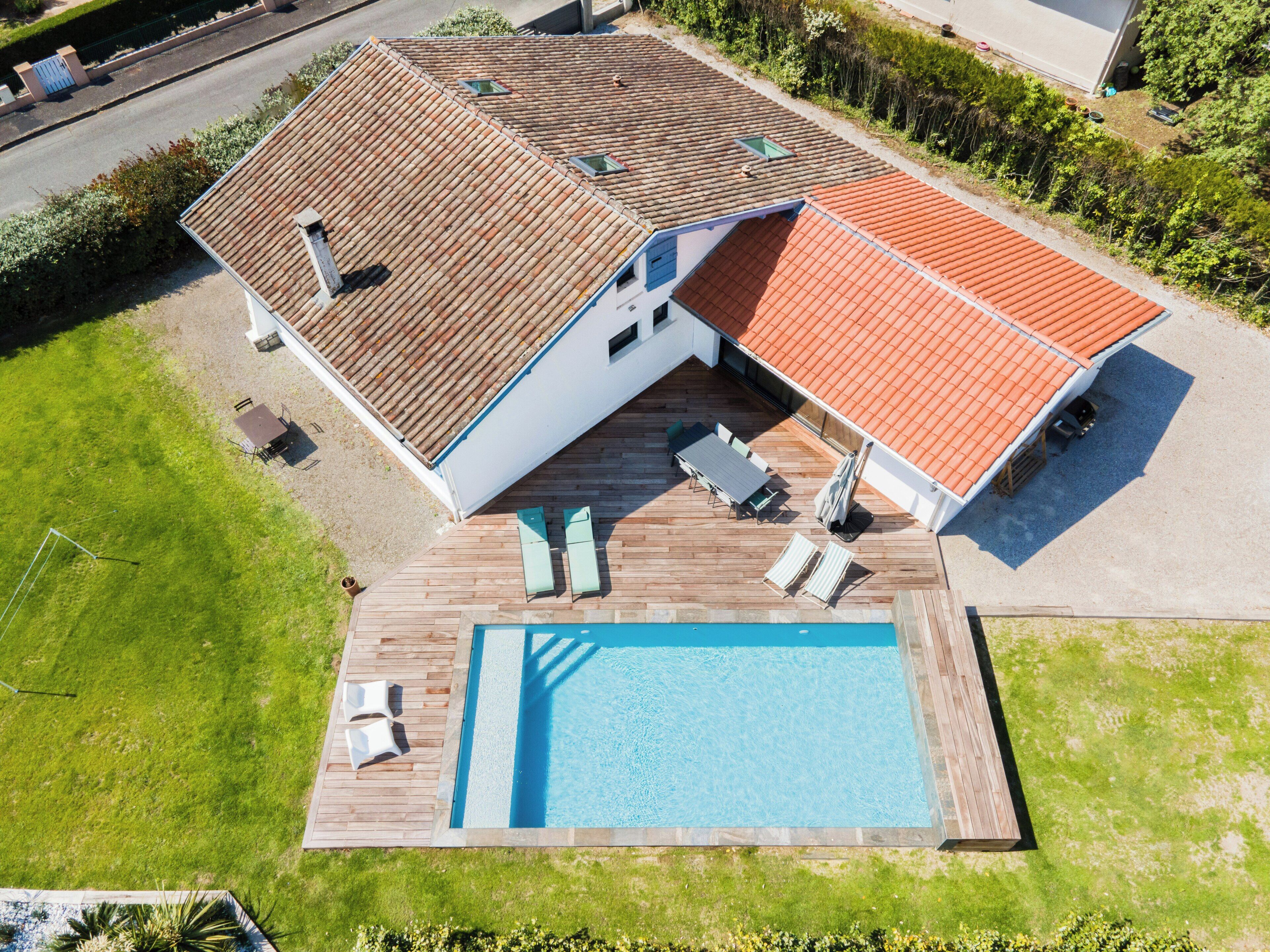 Una propiedad residencial con piscina, zona de terraza y techo de tejas rojas.