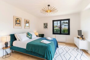 Ein modernes Schlafzimmer mit Bett, Nachttischlampen, einem Fenster mit Aussicht und Kunstwerken an den Wänden.