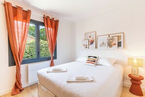 A bedroom with a bed, white bedding, a window with curtains, a bedside lamp, and wall art. - Beautiful Family villa in Seignosse (Seignosse)