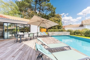 A wooden deck with lounge chairs and a table, a swimming pool, and a modern house with large windows. - Beautiful Family villa in Seignosse (Seignosse)