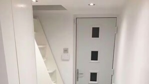Un pasillo estrecho con una puerta blanca, una escalera y un radiador.