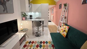 Un espacio habitable compacto con kitchenette, televisor, alfombra de diseño colorido y sofá verde.