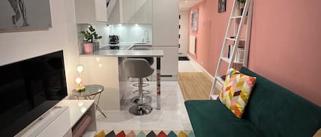 A compact living space with a kitchenette, a television, a colorful patterned rug, and a green sofa.