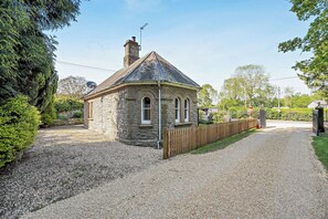 A stone building with a pitched roof, a wooden fence, and a gravel driveway. - The Lodge (Leominster)