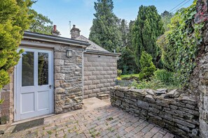 A stone cottage with a door, a small window, and a stone wall. - The Lodge (Leominster)