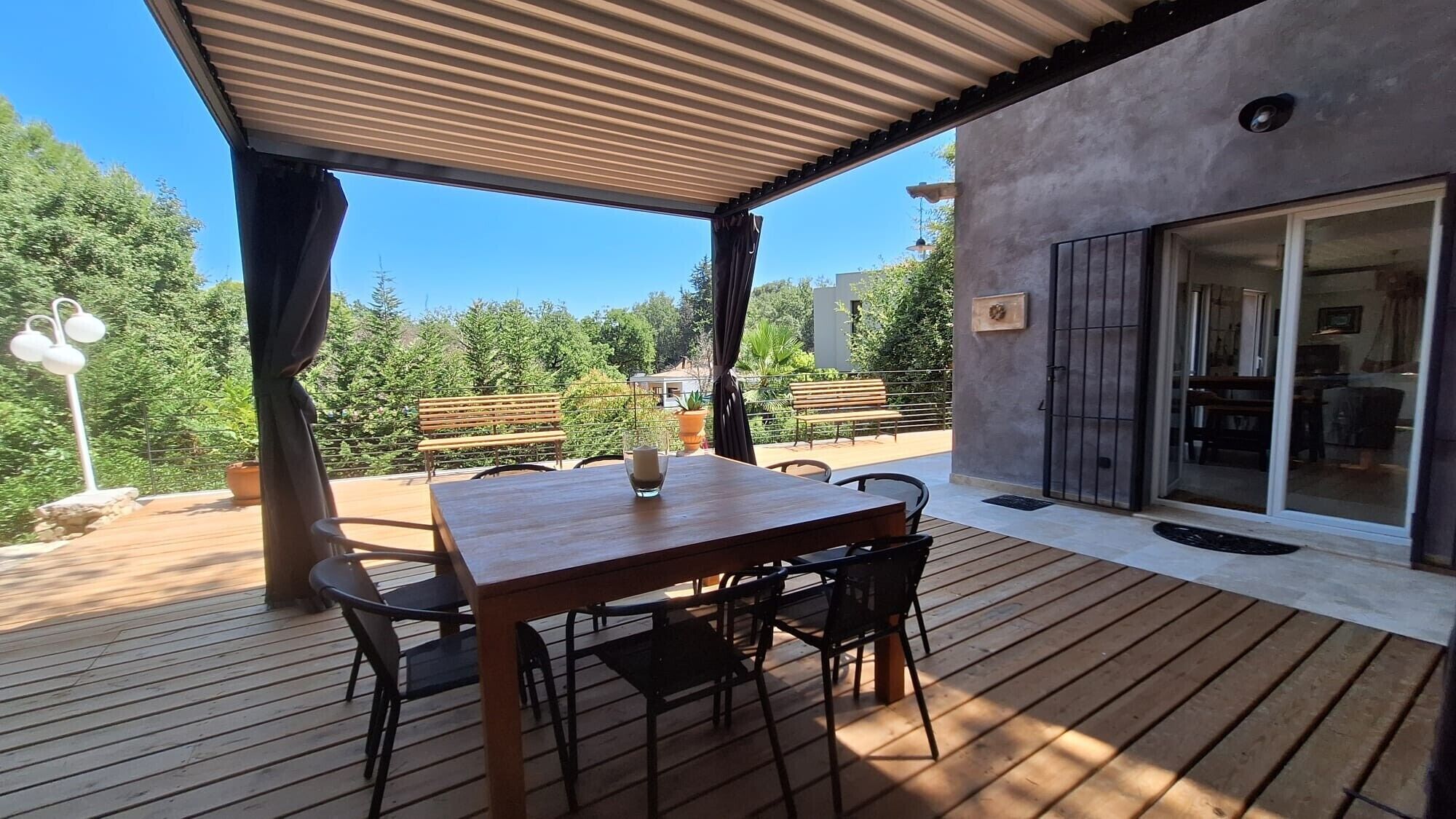 Une terrasse extérieure en bois, avec une table et des chaises, un banc et un pot de fleurs.