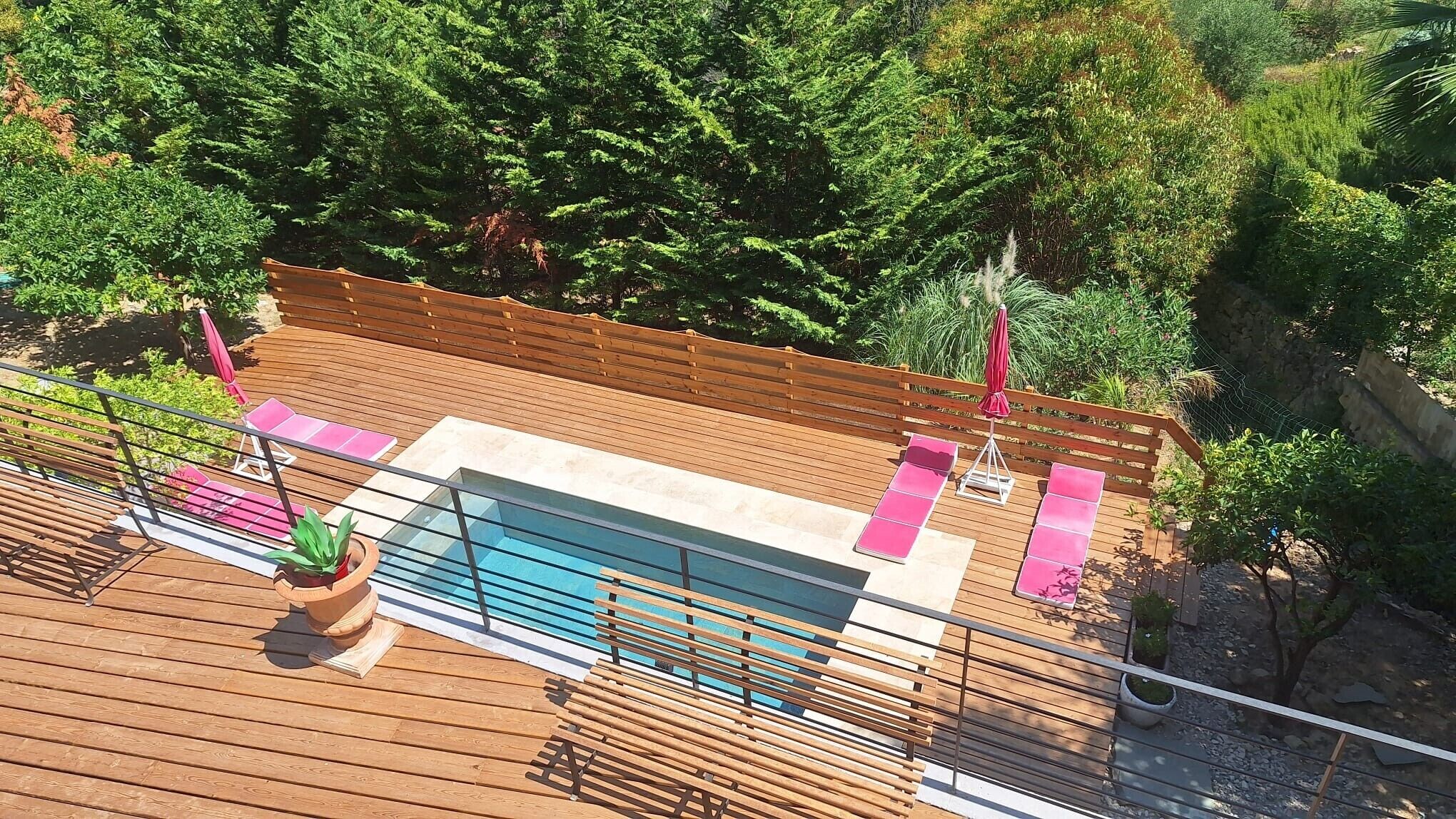 Une terrasse en bois avec une piscine, des chaises longues et une clôture en bois.