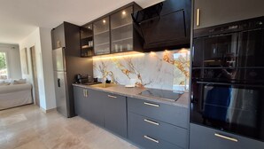 Eine moderne Küche mit dunklen Schränken, einer Marmor-Spritzschutzwand und einem eingebauten Backofen.