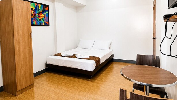 Una camera d'albergo con un letto, un armadio in legno, un quadro, una televisione e un tavolo da pranzo con sedie.