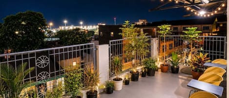A rooftop terrace with potted plants, outdoor seating, and string lights.