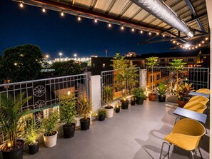Eine Dachterrasse mit Pflanzkübeln, Sitzgelegenheiten im Freien und Lichterketten.