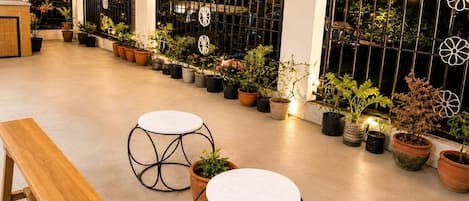 Une terrasse extérieure agrémentée de plantes en pot, d’un banc en bois et de deux tables rondes.