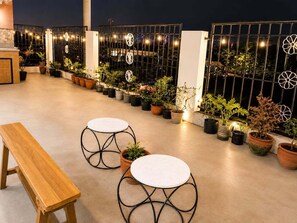 An outdoor terrace with potted plants, a wooden bench, and two round tables.