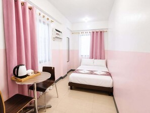 A hotel room with a bed, a small table with a kettle and a tray, a chair, and a window with curtains.