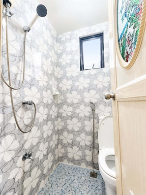 A bathroom with a shower, toilet, and a small window.
