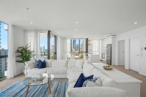 Ein modernes Wohnzimmer mit einem weißen Sofa, einem Glastisch und Blick auf die Stadtlandschaft.