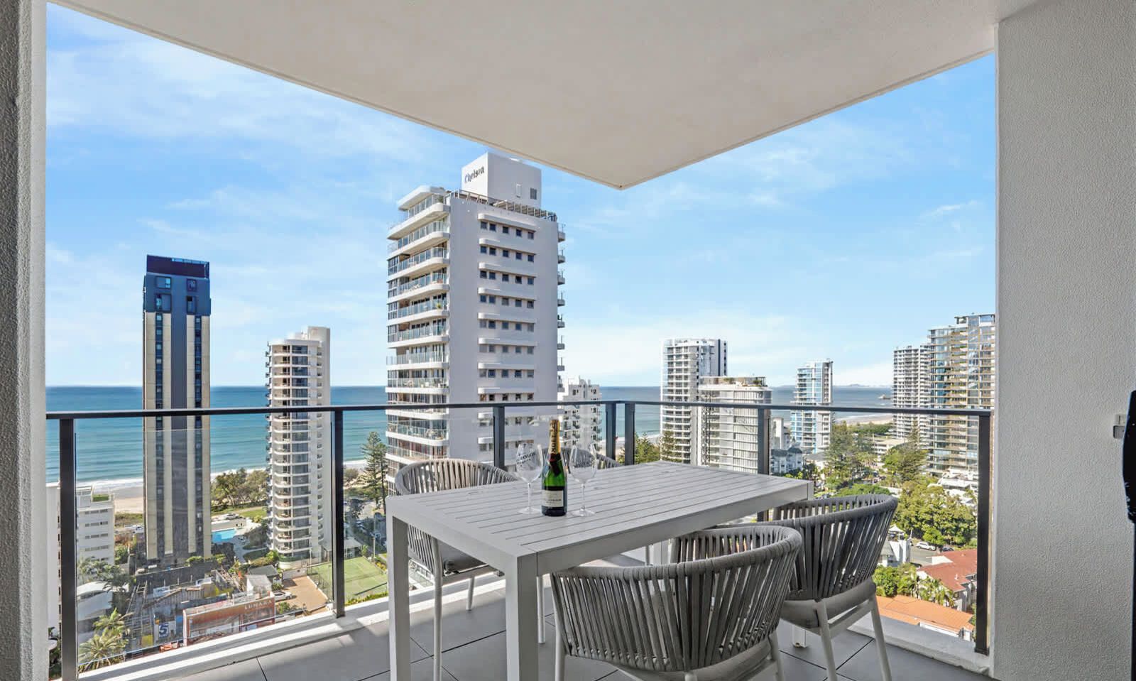 Varanda com mesa e cadeiras, com vista para a paisagem urbana e praia.