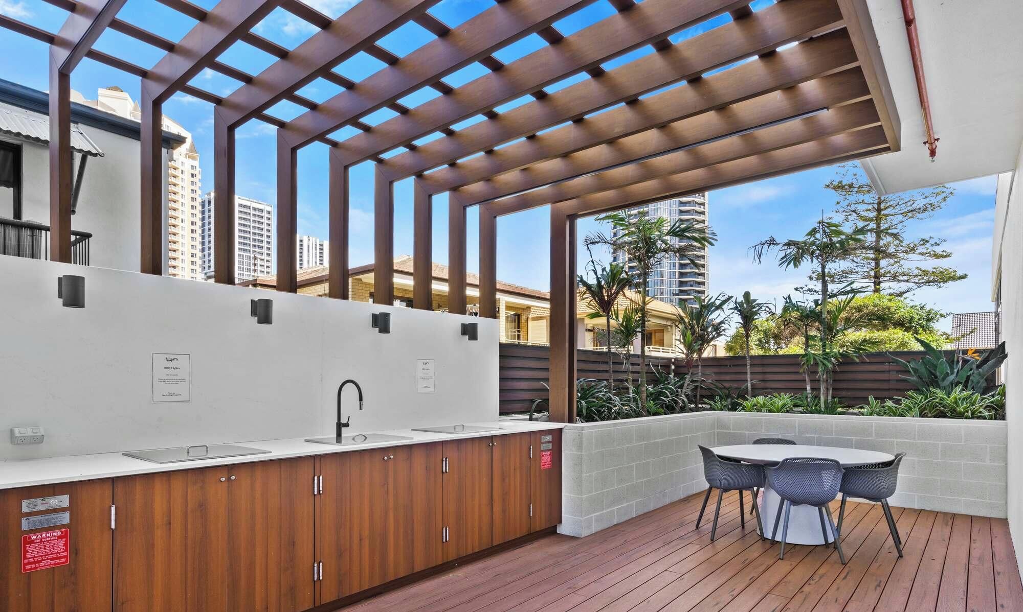 Un espace cuisine extérieur doté d’un évier encastré, de meubles en bois et d’une pergola au-dessus.