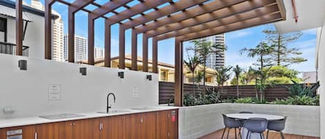 An outdoor kitchen area with a built-in sink, wooden cabinets, and a pergola overhead.
