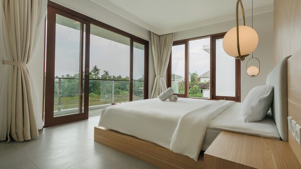 A modern bedroom with a large bed, a view of greenery outside, and a balcony. - Ombak D3 Villa by Betterplace (Cemagi)