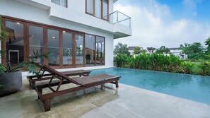 Ein modernes Haus mit Swimmingpool, Holzterrasse und Liegestühlen.