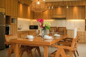 A modern kitchen with wooden cabinetry, a dining table set for six, and a hanging light fixture. - Ombak D3 Villa by Betterplace (Cemagi)