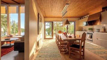 Een moderne keuken met houten kastjes, een eethoek met een grote tafel en stoelen, en uitzicht op het omliggende landschap door grote ramen.