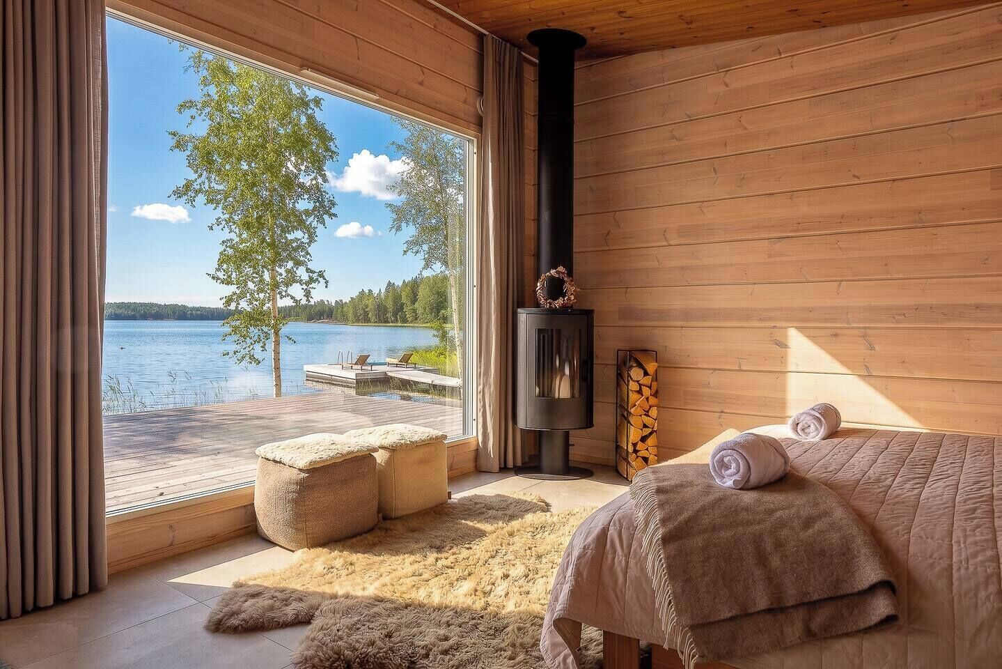 Een kamer met een groot raam met uitzicht op een meer, een open haard, een bed met opgerolde handdoeken en een houten vloer.