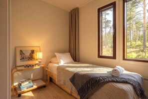 A bedroom with a bed, a bedside table with books, a lamp, and a window with a forest view. - Stay North - Viitala (Salo)