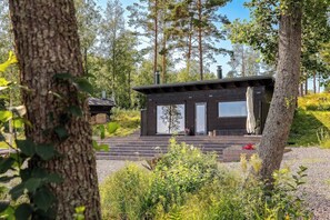 A cabin with a wooden exterior, a porch, and a window overlooking a forested area. - Stay North - Viitala (Salo)