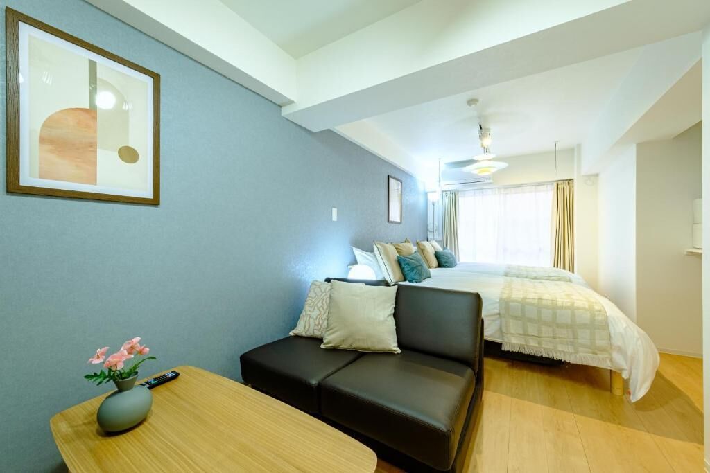 A hotel room with a bed, a sofa, a small table with a vase, and a framed picture on the wall.