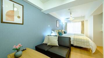 A hotel room with a bed, a sofa, a small table with a vase, and a framed picture on the wall.