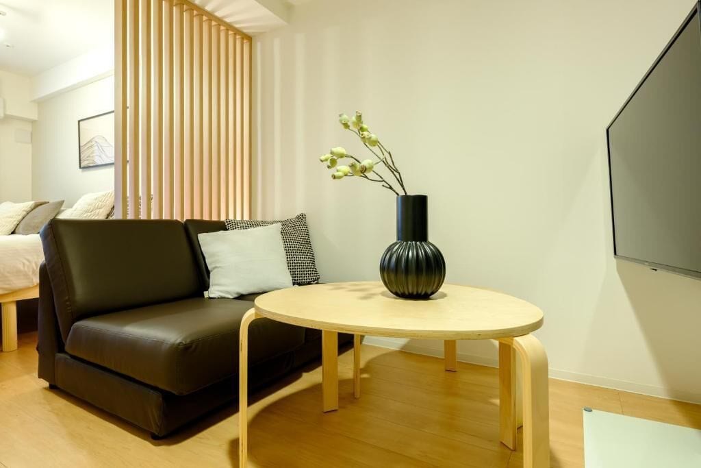 A modern living room with a sofa, a round wooden table, and a vase with flowers.