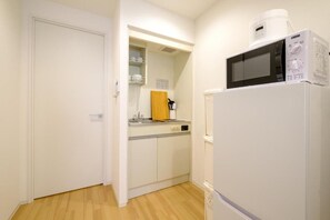 A compact kitchen with a microwave, refrigerator, and a wooden cutting board on the counter.