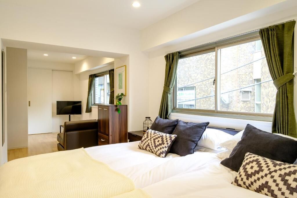 A hotel room with a bed, a TV, a desk, and a window with curtains.
