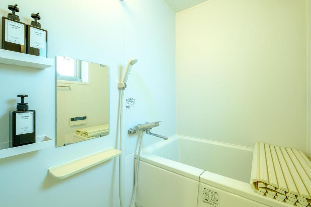 Un baño con bañera, ducha, espejo y estantes con artículos de aseo.