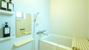 Un baño con bañera, ducha, espejo y estantes con artículos de aseo.