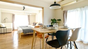 A well-lit hotel room with a wooden floor, a bed with a white headboard, a dining table set with plates and glasses, and a potted plant. - Choujamaru bill (Shinagawa-ku,Kamiosaki)