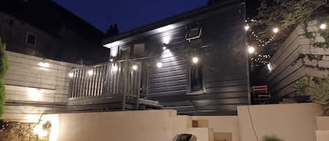 A modern two-story building with a balcony, outdoor seating, and string lights.