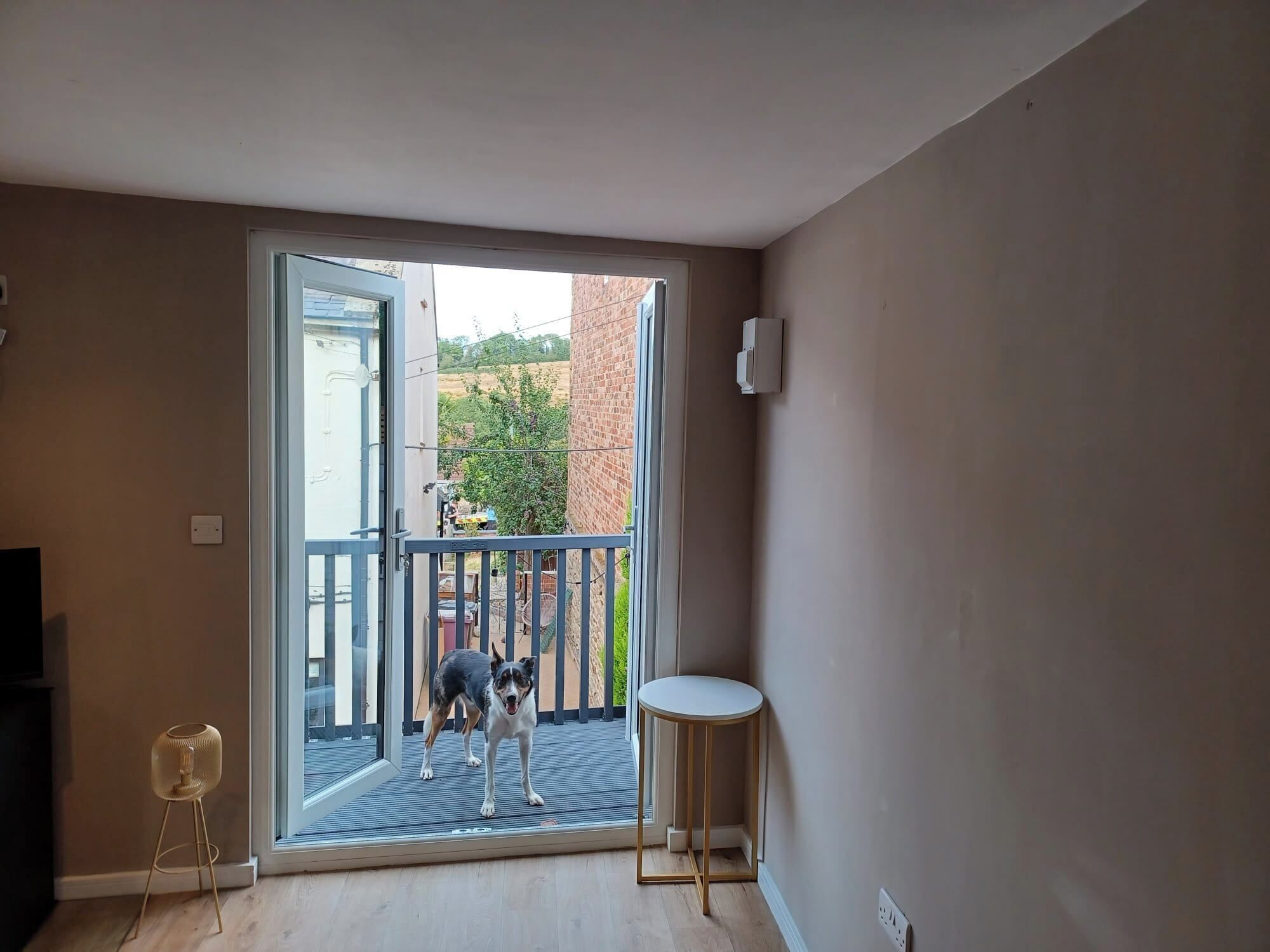 Una habitación con puerta corrediza de vidrio que da a un balcón, una pequeña mesa redonda y una lámpara de pie.