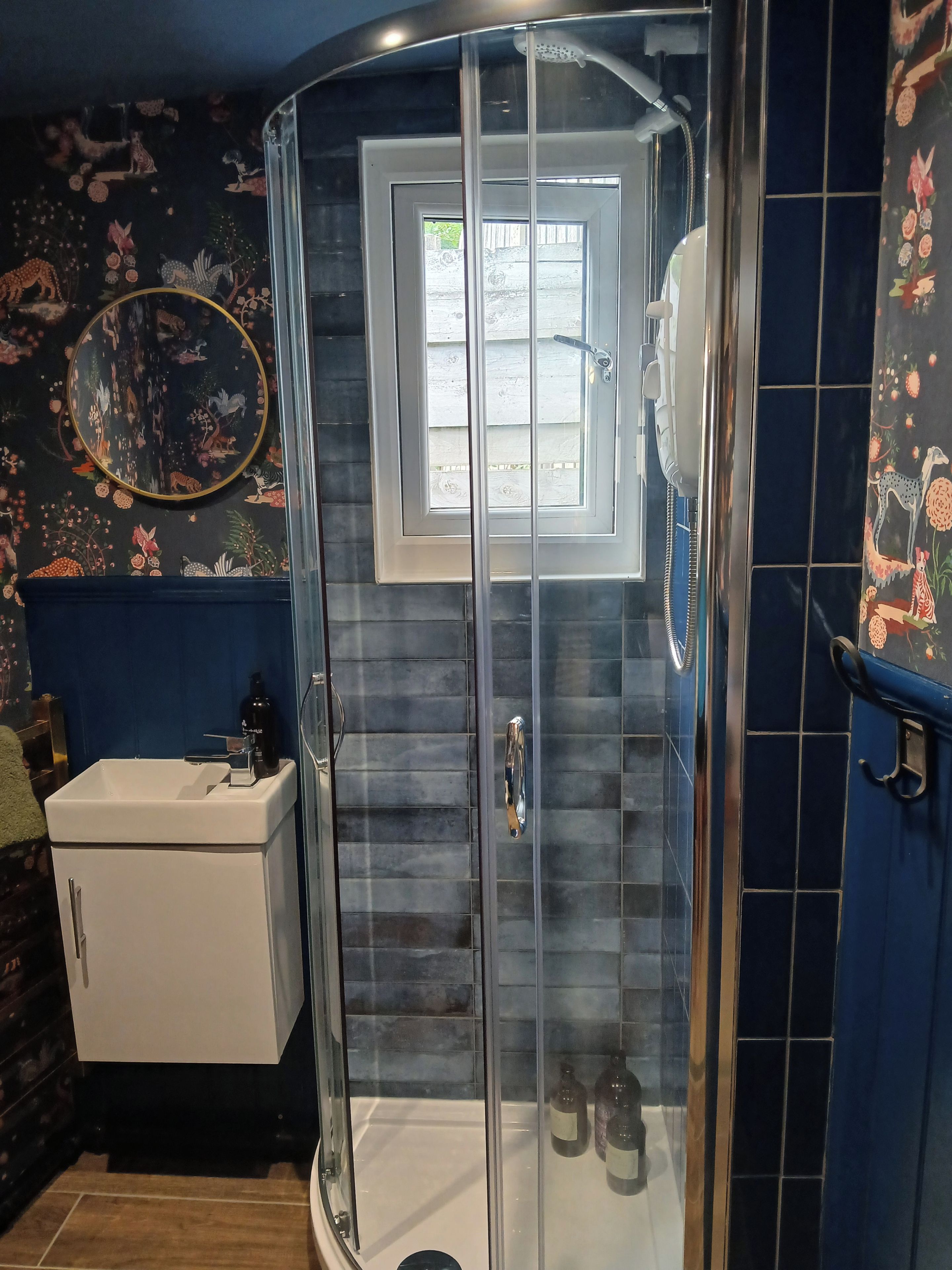 A bathroom with a glass shower enclosure, a white sink, and a decorative mirror.
