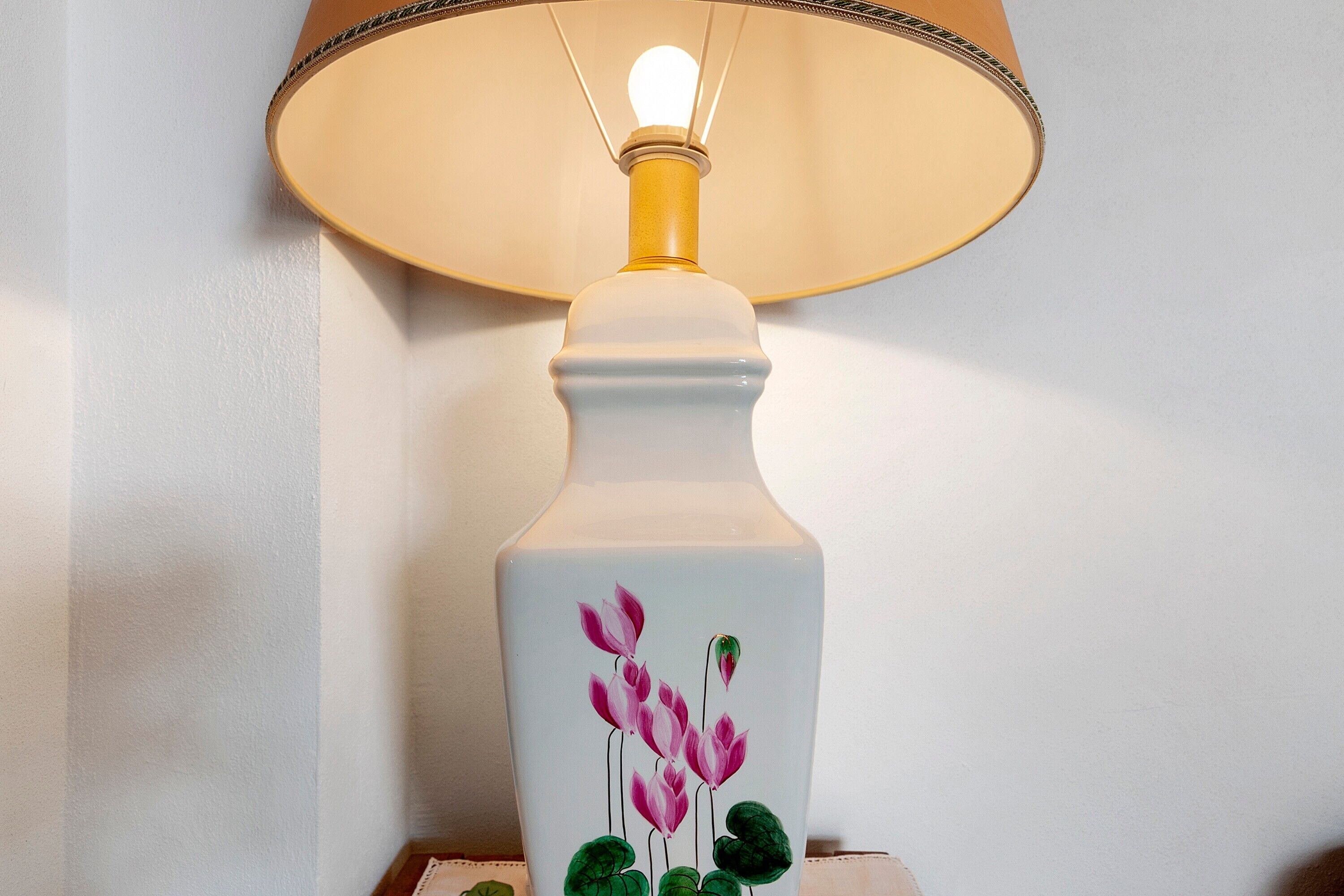 Una lámpara de mesa con pantalla blanca y un diseño floral en la base.