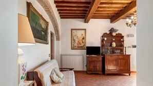 A room with a wooden ceiling, a sofa, a radiator, a television, and a cabinet with decorative items. - Rosmarinus Apartment – Two-Room Flat with Views of Tuscan Vineyards (San Casciano In Val di Pesa)