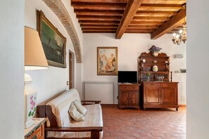 A room with a wooden ceiling, a sofa, a radiator, a television, and a cabinet with decorative items. - Rosmarinus Apartment – Two-Room Flat with Views of Tuscan Vineyards (San Casciano In Val di Pesa)